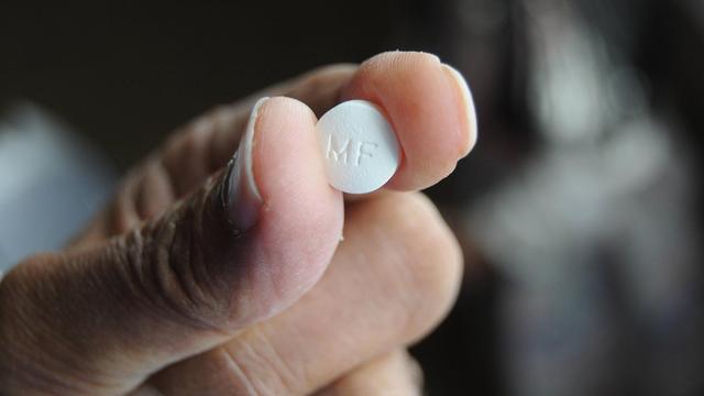 Eine Person hält eine Pille des Medikaments Metformin in der Hand