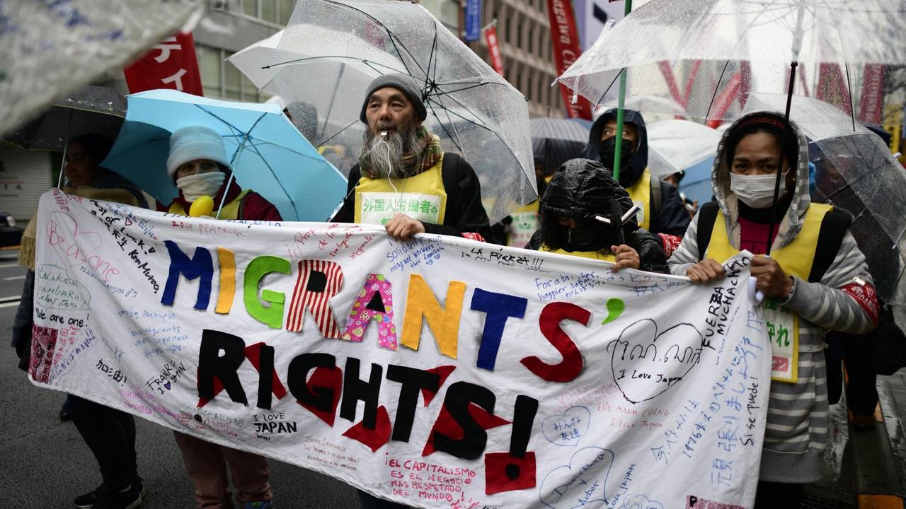 Demonstranten in Tokyo halten ein Plakat mit der Aufschrift "Migrants' Rights!". Demonstranten in Tokyo halten ein Plakat mit der Aufschrift "Migrants' Rights!".