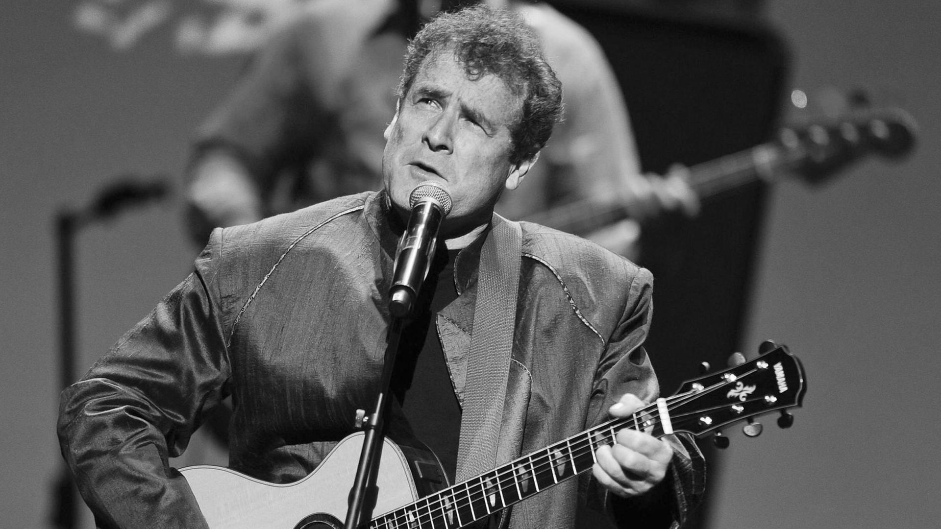 Der südafrikanische Sänger Johnny Clegg auf der Bühne mit einer Gitarre. Der südafrikanische Sänger Johnny Clegg auf der Bühne mit einer Gitarre.