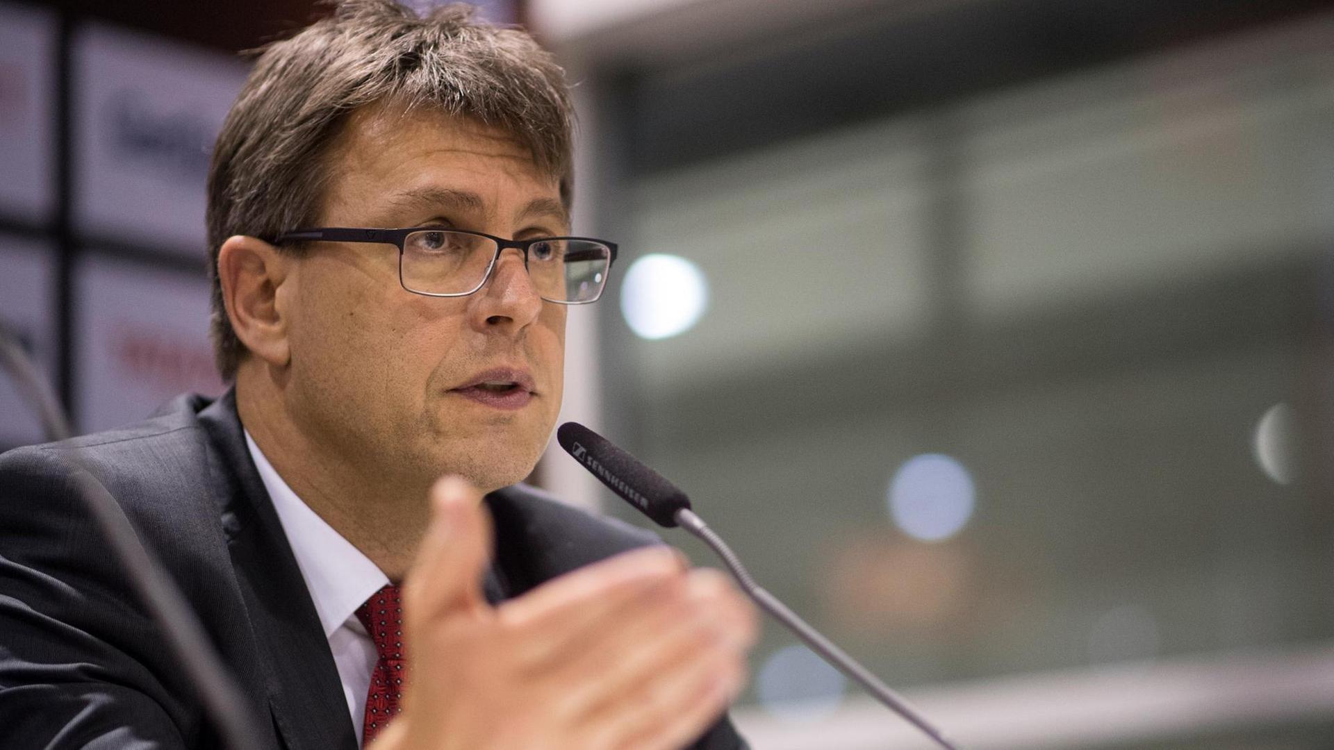 Weikert spricht ernst in ein Mikrofon und gestikuliert. Weikert spricht ernst in ein Mikrofon und gestikuliert.