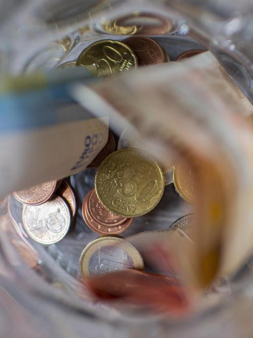 Münzgeld und Scheingeld liegen in einem Glasbehälter.