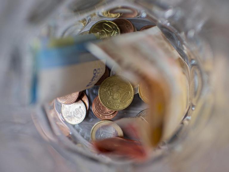 Münzgeld und Scheingeld liegen in einem Glasbehälter.