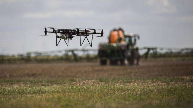 Eine Drohne fliegt über einem Feld mit einem Traktor mit Anhängespritze, aufgenommen auf einem 5G-Testfeld auf dem Lehr- und Versuchsgut (LVG) in Koellitsch