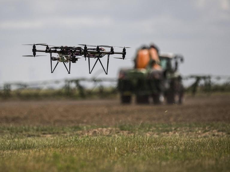 Eine Drohne fliegt über einem Feld mit einem Traktor mit Anhängespritze, aufgenommen auf einem 5G-Testfeld auf dem Lehr- und Versuchsgut (LVG) in Koellitsch