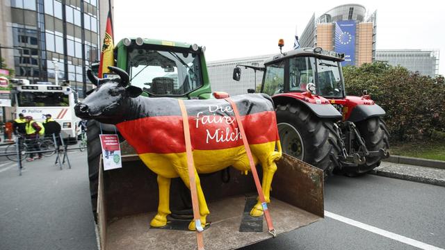 Ein Traktor fährt eine Kuh-Statue in schwarz-rot-gold durch das EU-Viertel in Brüssel. Auf der Kuh steht "Die faire Milch":