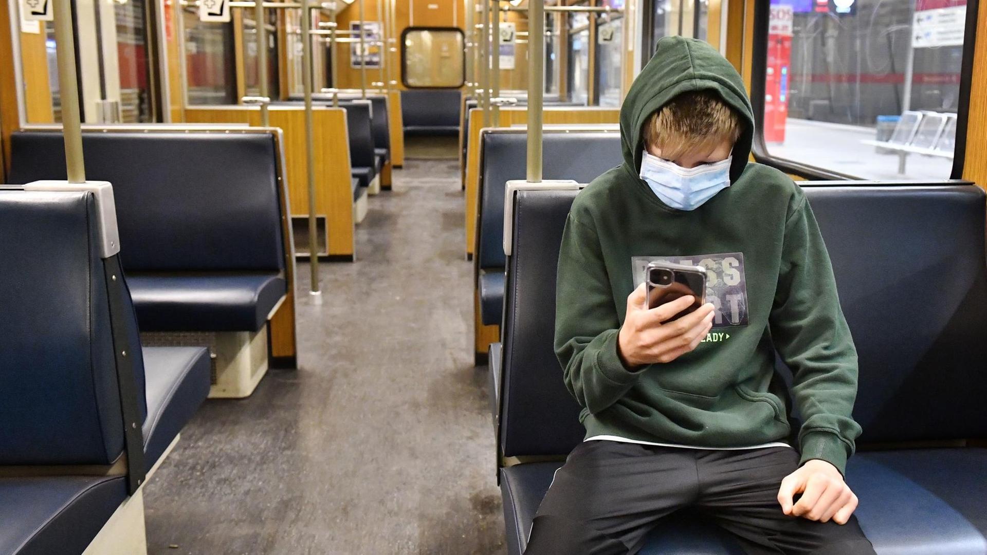 Ein Jugendlicher ist in einer leeren U-Bahn in München unterwegs und blickt auf sein Smartphone. Ein Jugendlicher ist in einer leeren U-Bahn in München unterwegs und blickt auf sein Smartphone.