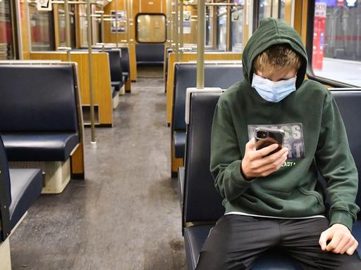 Ein Jugendlicher ist in einer leeren U-Bahn in München unterwegs und blickt auf sein Smartphone.
