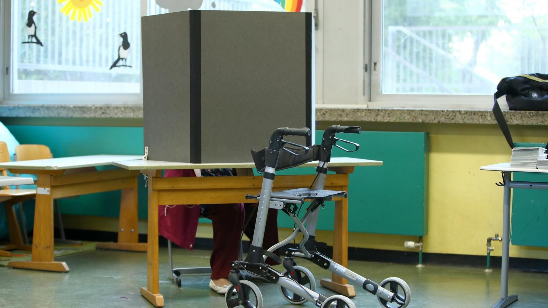 Eine Frau hat ihren Rollator vor die Wahlkabine in einer Schule gestellt.