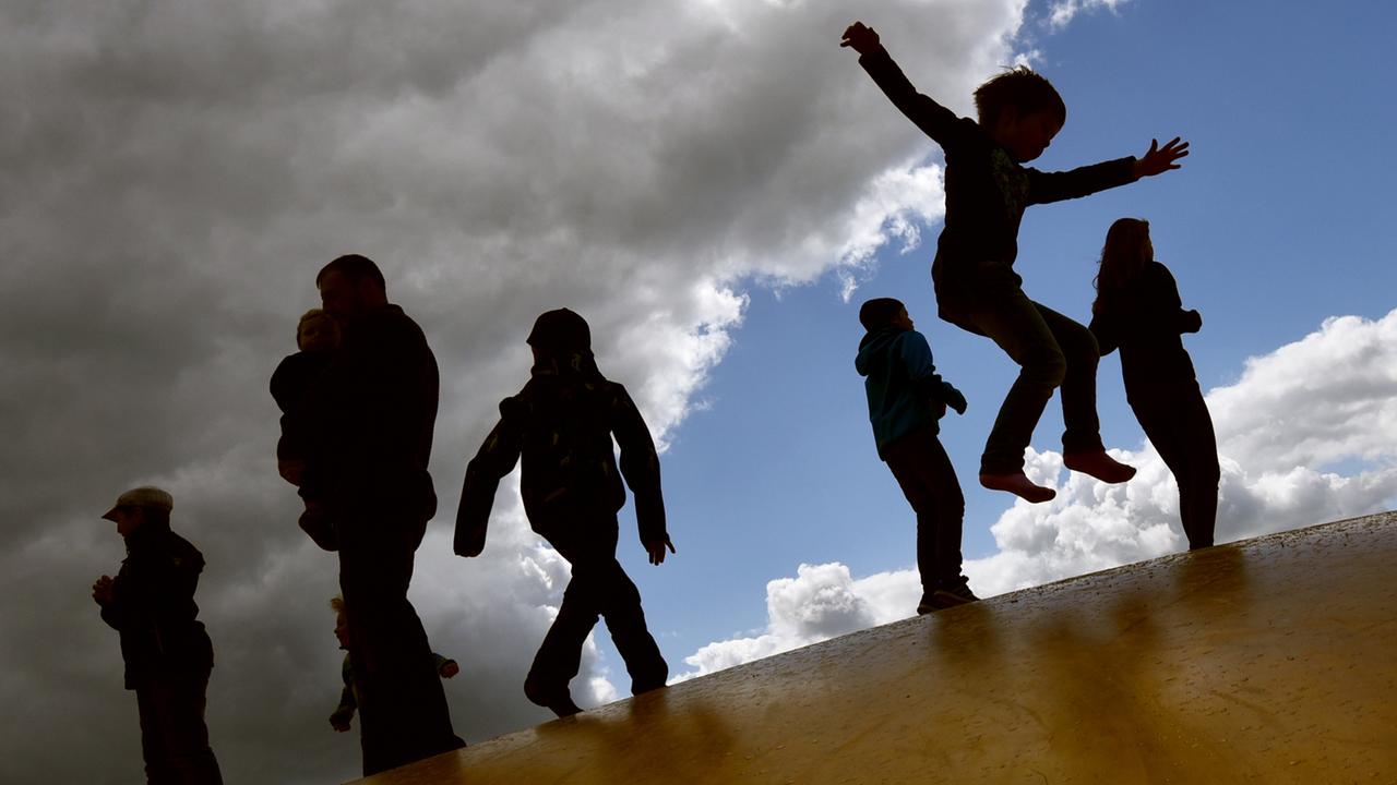 Kinder springen am 17.05.2015 bei wechselhaftem Wetter auf einer Hüpfburg in Elstal (Brandenburg) und heben sich dabei als Schatten vom Himmel ab. 