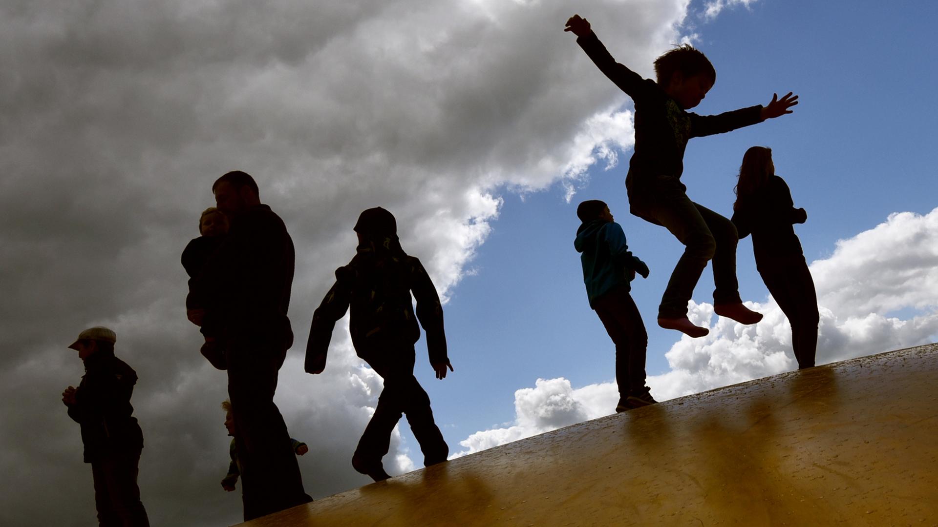 Kinder springen am 17.05.2015 bei wechselhaftem Wetter auf einer Hüpfburg in Elstal (Brandenburg) und heben sich dabei als Schatten vom Himmel ab.