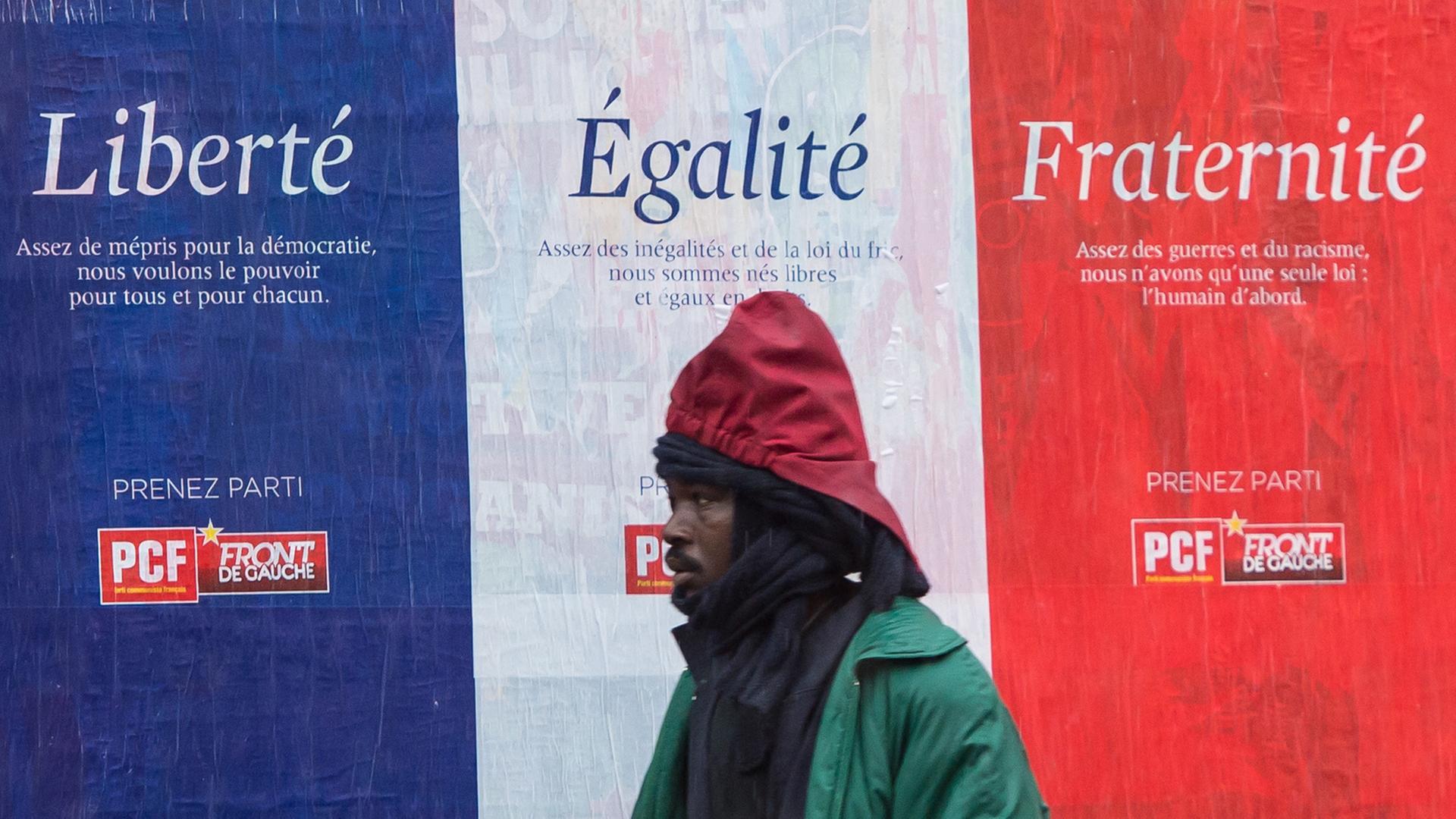 Ein Migrant geht vor einem Plakat mit den Worten "Liberé, Égalité, Fraternité" in Calais. Ein Migrant geht vor einem Plakat mit den Worten "Liberé, Égalité, Fraternité" in Calais.