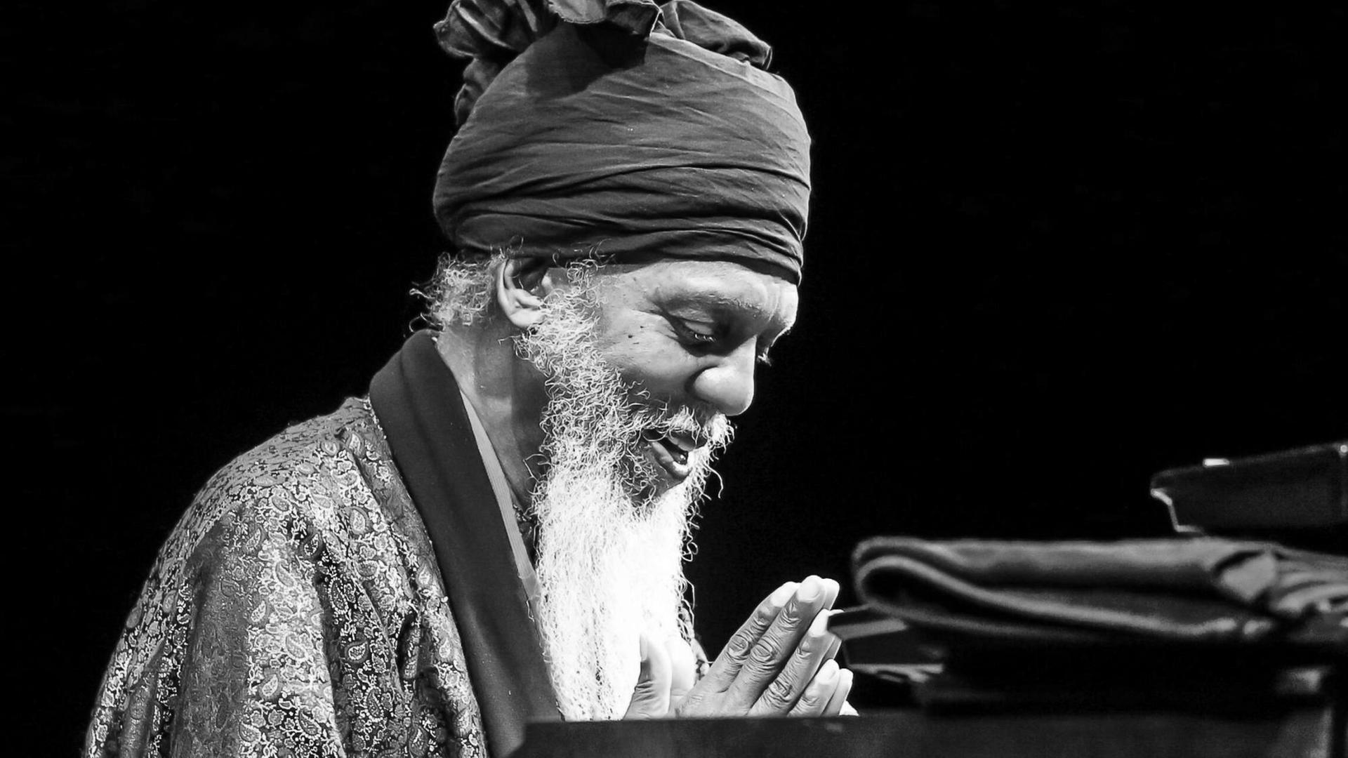 Mit Turban und weißem Bart, die Hände gefaltet, die Augen geschlossen sitzt Dr. Lonnie Smith vor seiner Orgel. Mit Turban und weißem Bart, die Hände gefaltet, die Augen geschlossen sitzt Dr. Lonnie Smith vor seiner Orgel.