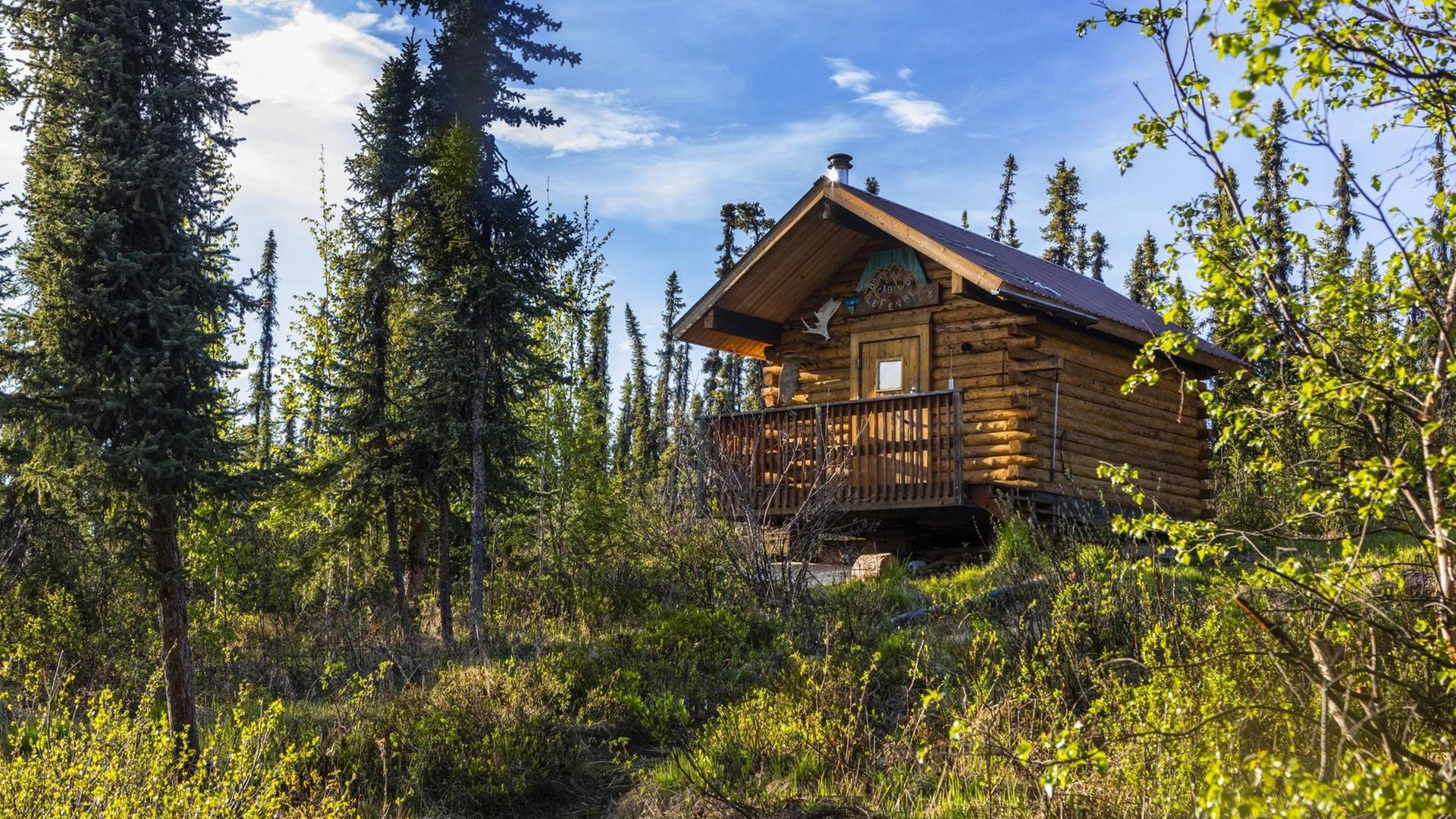 Eine Holzhütte steht abgeschieden in einem Wald in Alaska. Eine Holzhütte steht abgeschieden in einem Wald in Alaska.