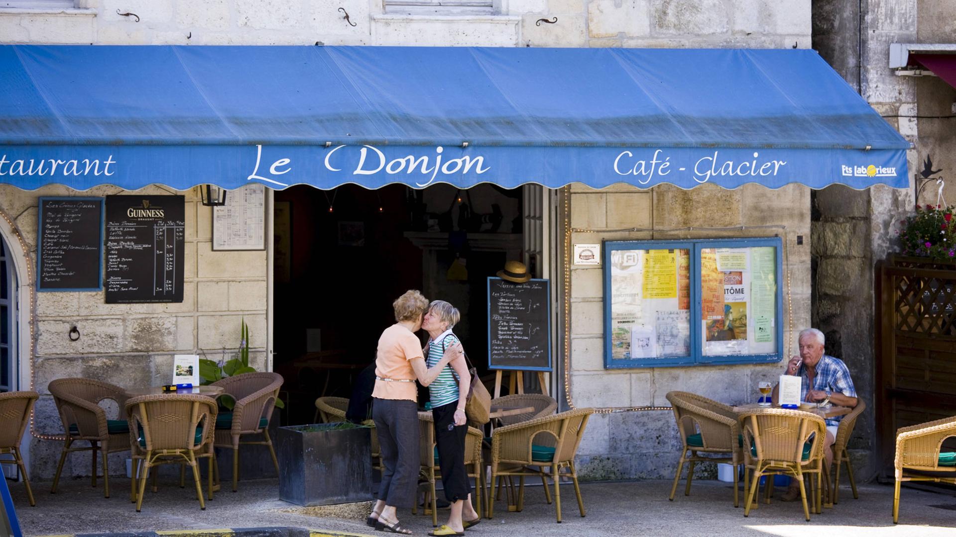 Zwei Frauen begrüßen sich vor einem Restaurant in Bourdeilles, Frankreich.