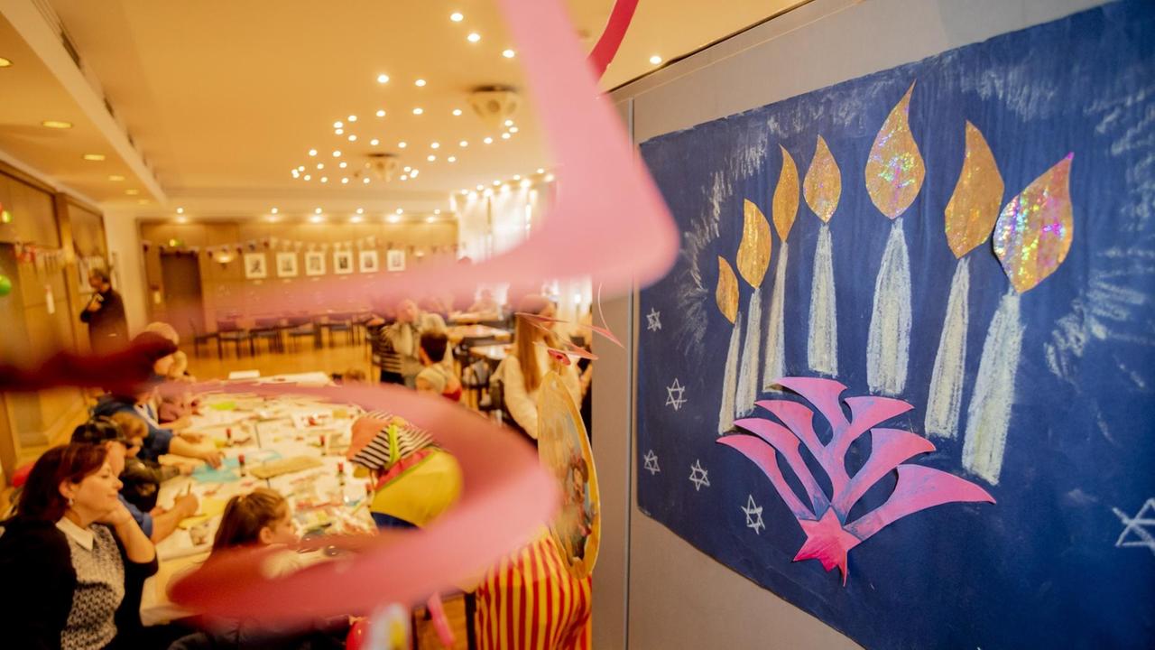 Ein Bild eines Chanukkaleuchters hängt beim Balagan Day im Jüdischen Gemeindehaus an einer Tür, während im Hintergrund Kinder basteln. Im Rahmen der Jüdischen Kulturtagen Berlin lädt das Jüdische Gemeindehaus zum Tag der offenen Tür ein. Ein Bild eines Chanukkaleuchters hängt beim Balagan Day im Jüdischen Gemeindehaus an einer Tür, während im Hintergrund Kinder basteln. Im Rahmen der Jüdischen Kulturtagen Berlin lädt das Jüdische Gemeindehaus zum Tag der offenen Tür ein.