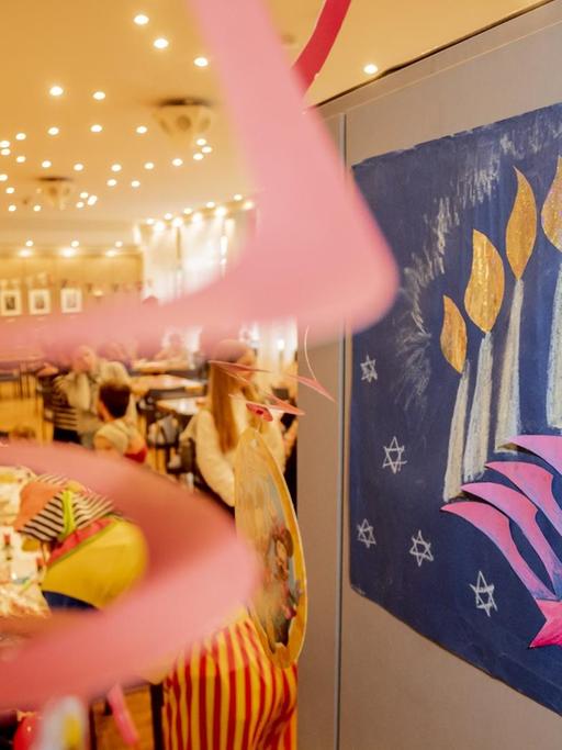 Ein Bild eines Chanukkaleuchters hängt beim Balagan Day im Jüdischen Gemeindehaus an einer Tür, während im Hintergrund Kinder basteln. Im Rahmen der Jüdischen Kulturtagen Berlin lädt das Jüdische Gemeindehaus zum Tag der offenen Tür ein.