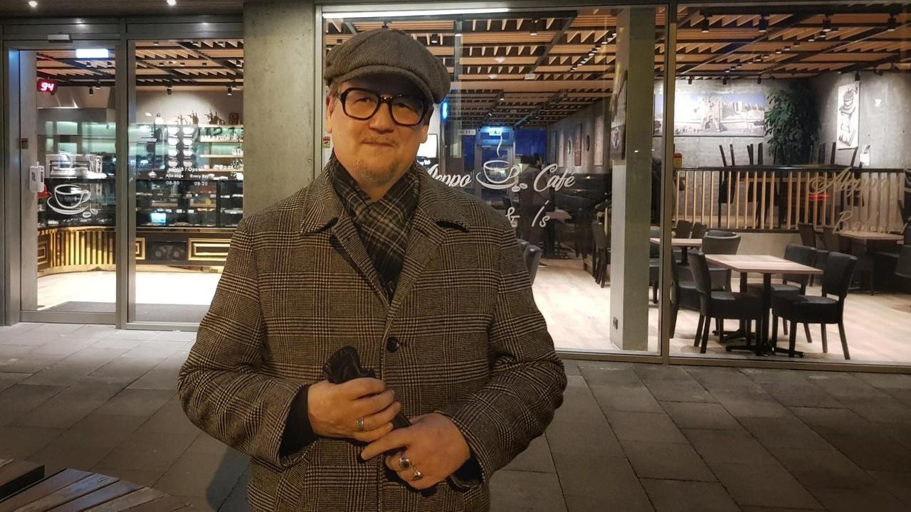 Der isländische Autor Sjón mit Mütze und Mantel vor einem Cafe