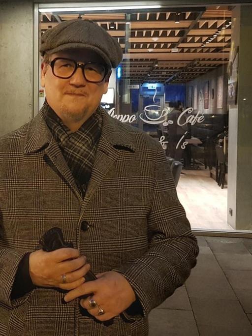 Der isländische Autor Sjón mit Mütze und Mantel vor einem Cafe