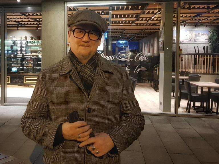 Der isländische Autor Sjón mit Mütze und Mantel vor einem Cafe