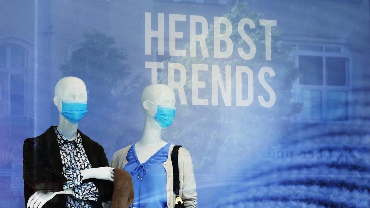 Zwei Schaufensterpuppen stehen im Schaufenstermit Masken da. Im Hintergrund steht der Schriftzug "Herbst Trends". Zwei Schaufensterpuppen stehen im Schaufenstermit Masken da. Im Hintergrund steht der Schriftzug "Herbst Trends".