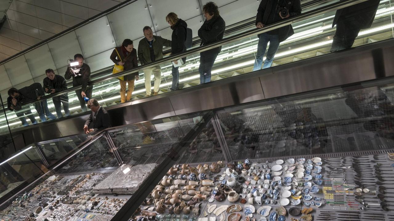 Menschen fahren auf der Rolltreppe hinab in die Rokin Metro-Station in Amsterdam. Daneben sind in Glaskästen die archäologischen Funde des Projekts "Below the Surface" ausgestellt. Menschen fahren auf der Rolltreppe hinab in die Rokin Metro-Station in Amsterdam. Daneben sind in Glaskästen die archäologischen Funde des Projekts "Below the Surface" ausgestellt.
