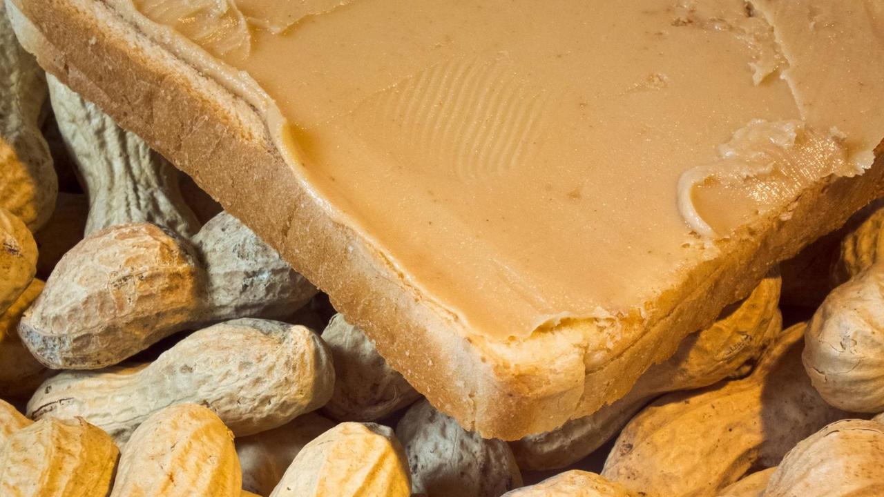 Ein mit Erdnussbutter bestrichener Toast vor einem Haufen Erdnüssen. Ein mit Erdnussbutter bestrichener Toast vor einem Haufen Erdnüssen.