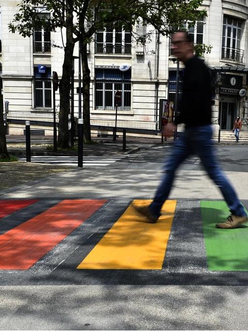 Ein Passant überquert einen Zebrastreifen in den Farben des Regenbogens.