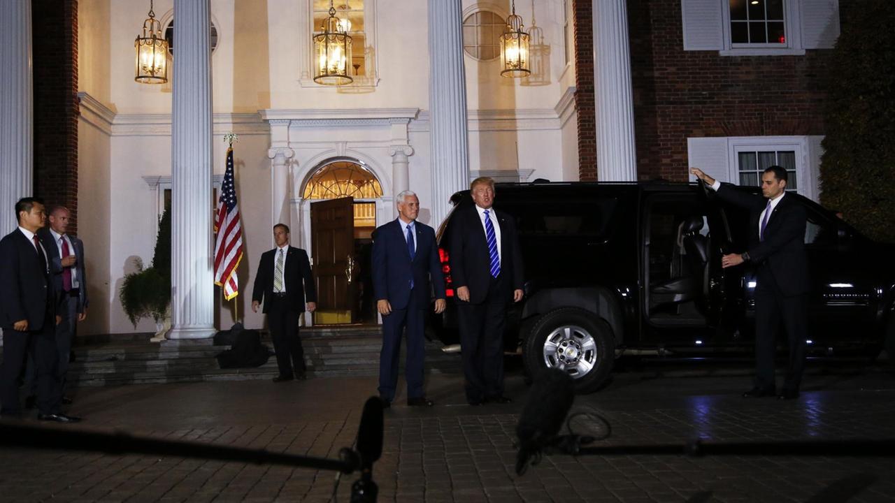 Sie sehen den designierten US-Präsidenten Trump und seinen angehenden Vize, sie kommen aus einem Haus, es ist dunkel draußen.