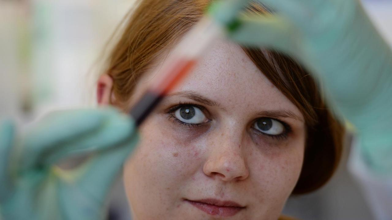 Die rothaarige Frau hält ein Röhrchen mit der Blutprobe gegen das Licht. Die rothaarige Frau hält ein Röhrchen mit der Blutprobe gegen das Licht.