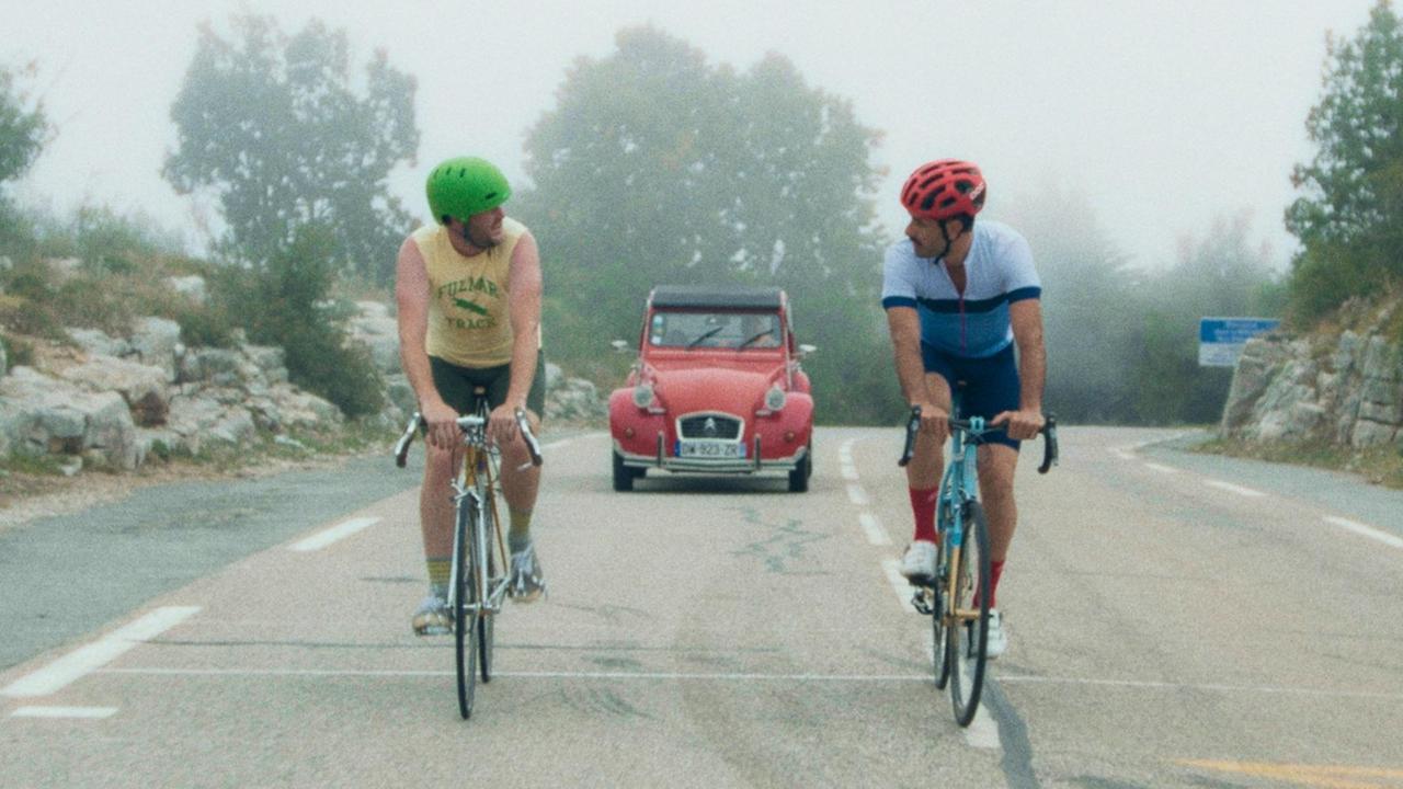 Kyle (Kyle Marvin, l.) und Mike (Michael Angelo Convino) unterhalten sich beim Rennradfahren. Im Hintergrund ist ein roter Citroen (Ente) zu sehen. Kyle (Kyle Marvin, l.) und Mike (Michael Angelo Convino) unterhalten sich beim Rennradfahren. Im Hintergrund ist ein roter Citroen (Ente) zu sehen.