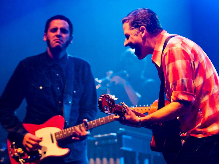 Zwei Männer stehen auf einer Bühne und spielen Gitarre.