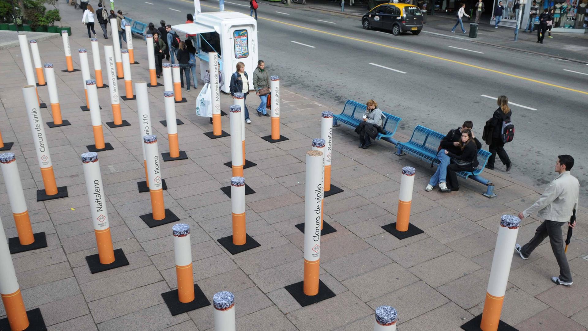 Eine Installation aus überdimensionalen Zigaretten steht auf einem belebten Platz. Eine Installation aus überdimensionalen Zigaretten steht auf einem belebten Platz.