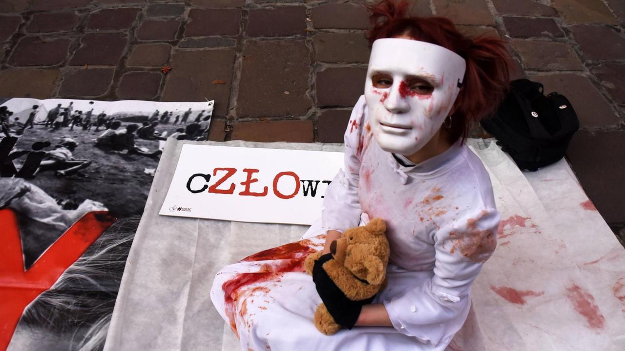 Darstellerin sitzt mit Maske, blutverschmiertem Kittel und Teddybär auf dem Asphalt vor dem Bischofspalast in Krakau am 22. November Darstellerin sitzt mit Maske, blutverschmiertem Kittel und Teddybär auf dem Asphalt vor dem Bischofspalast in Krakau am 22. November