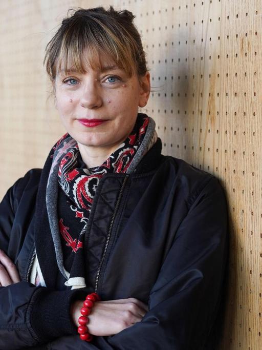 Yvonne Büdenhölzer, Leiterin des Berliner Theatertreffens, steht mit verschränkten Armen vor einer Holzwand.