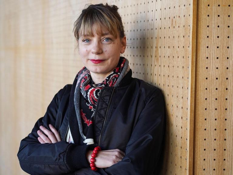 Yvonne Büdenhölzer, Leiterin des Berliner Theatertreffens, steht mit verschränkten Armen vor einer Holzwand.