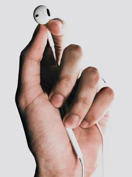 Fotografie einer Hand, die einen weißen In-Ear-Kopfhörer  zwischen Daumen und Zeigenfinder hält.