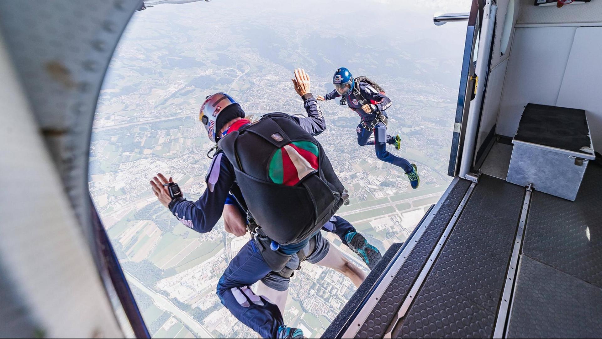 Drei Personen mit Fallschirmen springen aus einem Flugzeug. Unten sieht man eine bebaute Landschaft. Drei Personen mit Fallschirmen springen aus einem Flugzeug. Unten sieht man eine bebaute Landschaft.