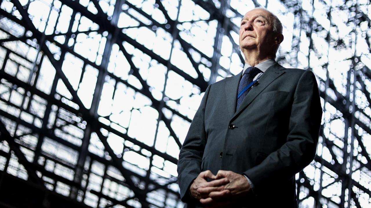 Porträt von Gilles de Kerchove, der mit gefalteten Händen vor einer Glasfassade steht. Porträt von Gilles de Kerchove, der mit gefalteten Händen vor einer Glasfassade steht.