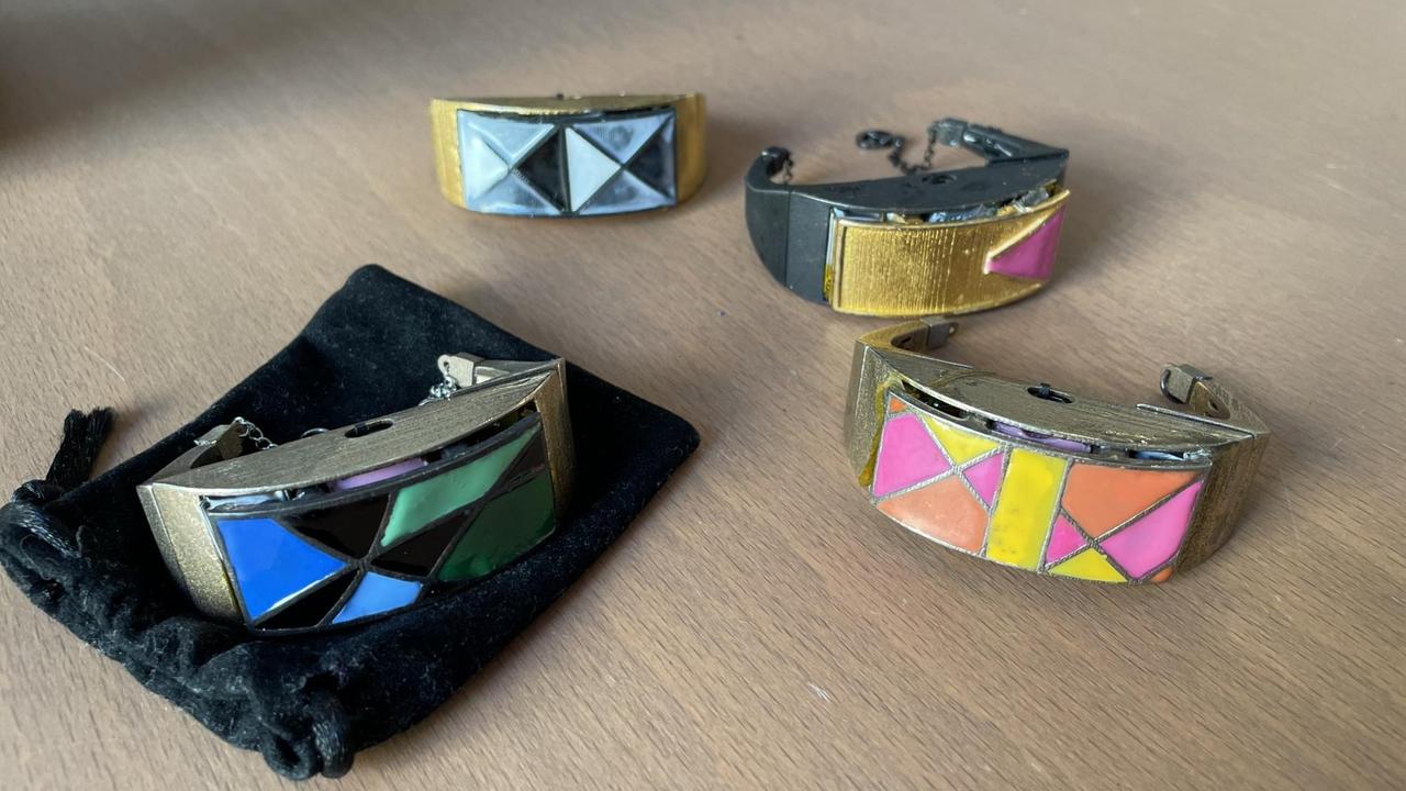 Auf einer glatten Fläche liegen mehrere bunt angemalte, breite Messingarmbänder. Auf einer glatten Fläche liegen mehrere bunt angemalte, breite Messingarmbänder.