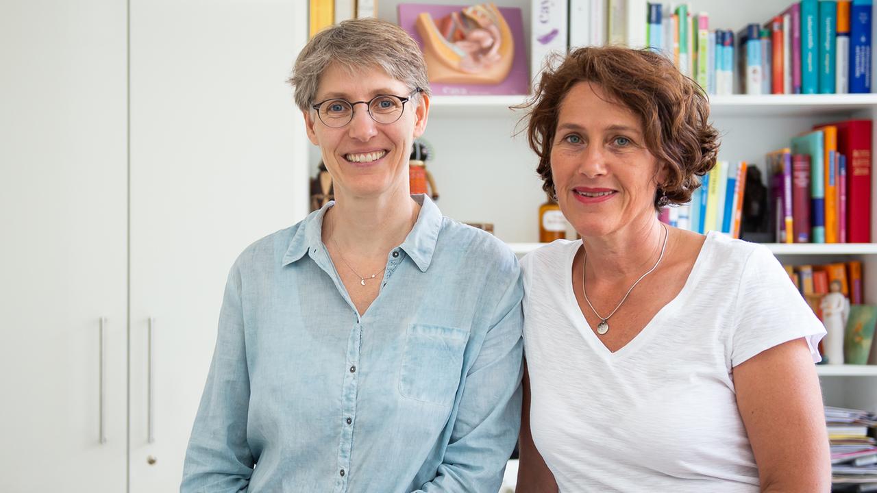 Die Frauenärztinnen Natascha Nicklaus (l.) und Nora Szász stehen vor einer Bücherwand und lächeln. Die Frauenärztinnen Natascha Nicklaus (l.) und Nora Szász stehen vor einer Bücherwand und lächeln.