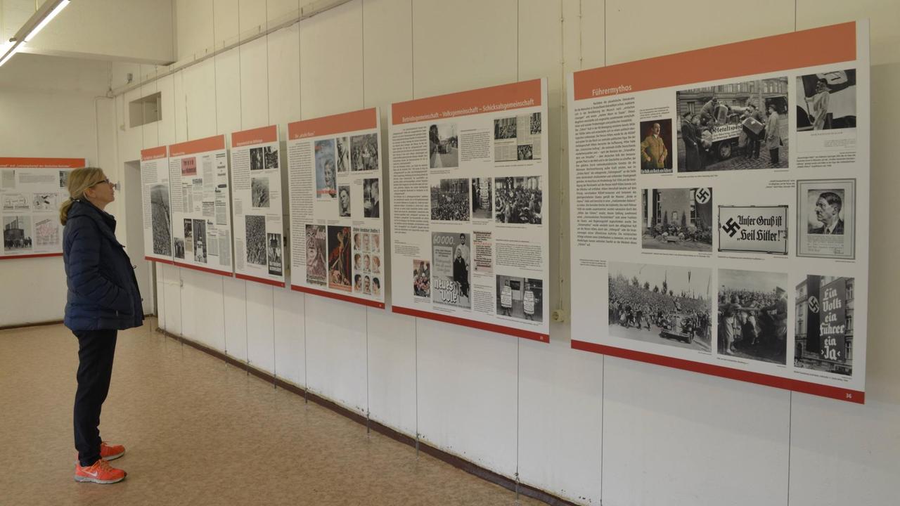 Eine Frau steht vor einer Wand und betrachtet die Ausstellungsinhalte. Eine Frau steht vor einer Wand und betrachtet die Ausstellungsinhalte.