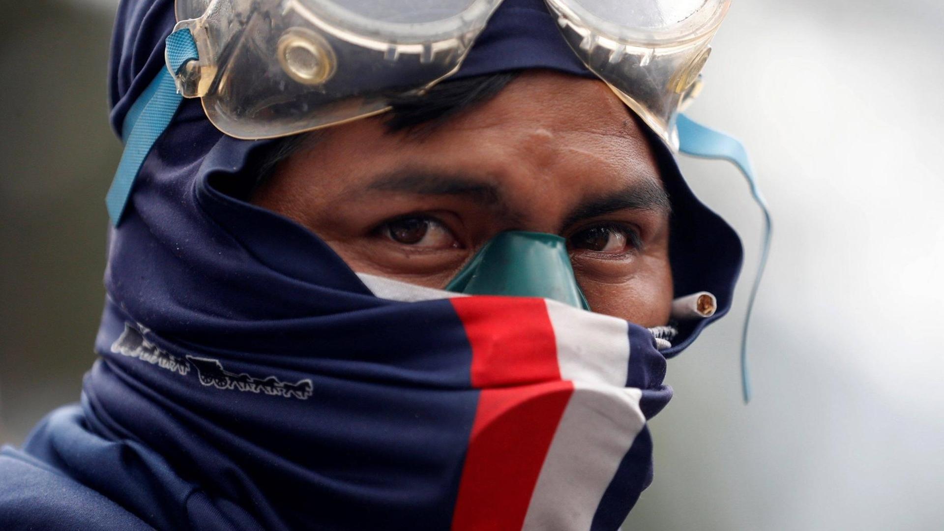 Großaufnahme eines verhüllten Demonstranten mit Schutzbrille auf der Stirn, der ernst und entschlossen ins Off des Bildes blickt.