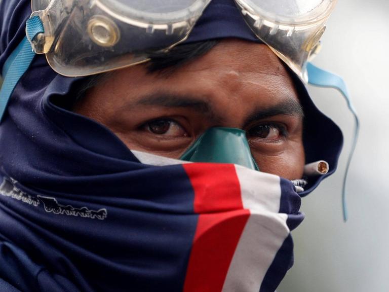 Großaufnahme eines verhüllten Demonstranten mit Schutzbrille auf der Stirn, der ernst und entschlossen ins Off des Bildes blickt.
