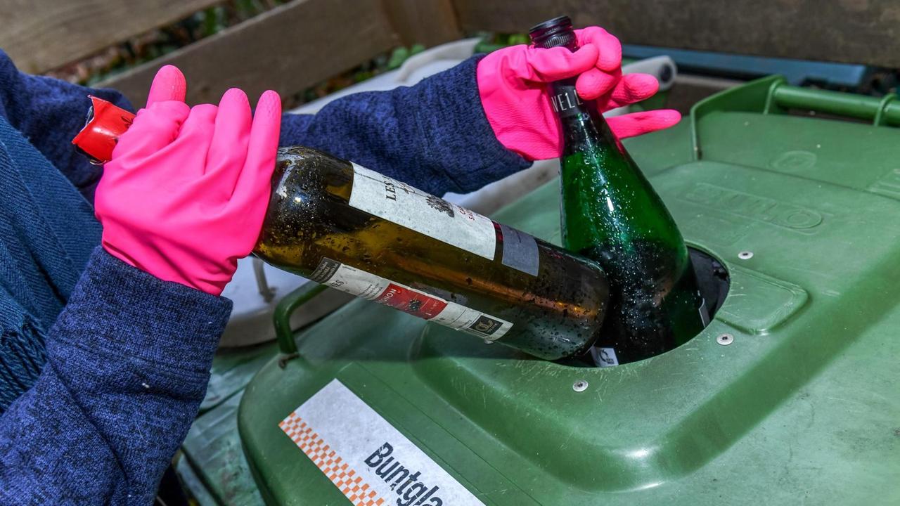Eine Person mit pinken Gummihandschuhen wirft Flaschen in eine Altglastonne für Buntglas, aufgenommen 2019 in Berlin Eine Person mit pinken Gummihandschuhen wirft Flaschen in eine Altglastonne für Buntglas, aufgenommen 2019 in Berlin