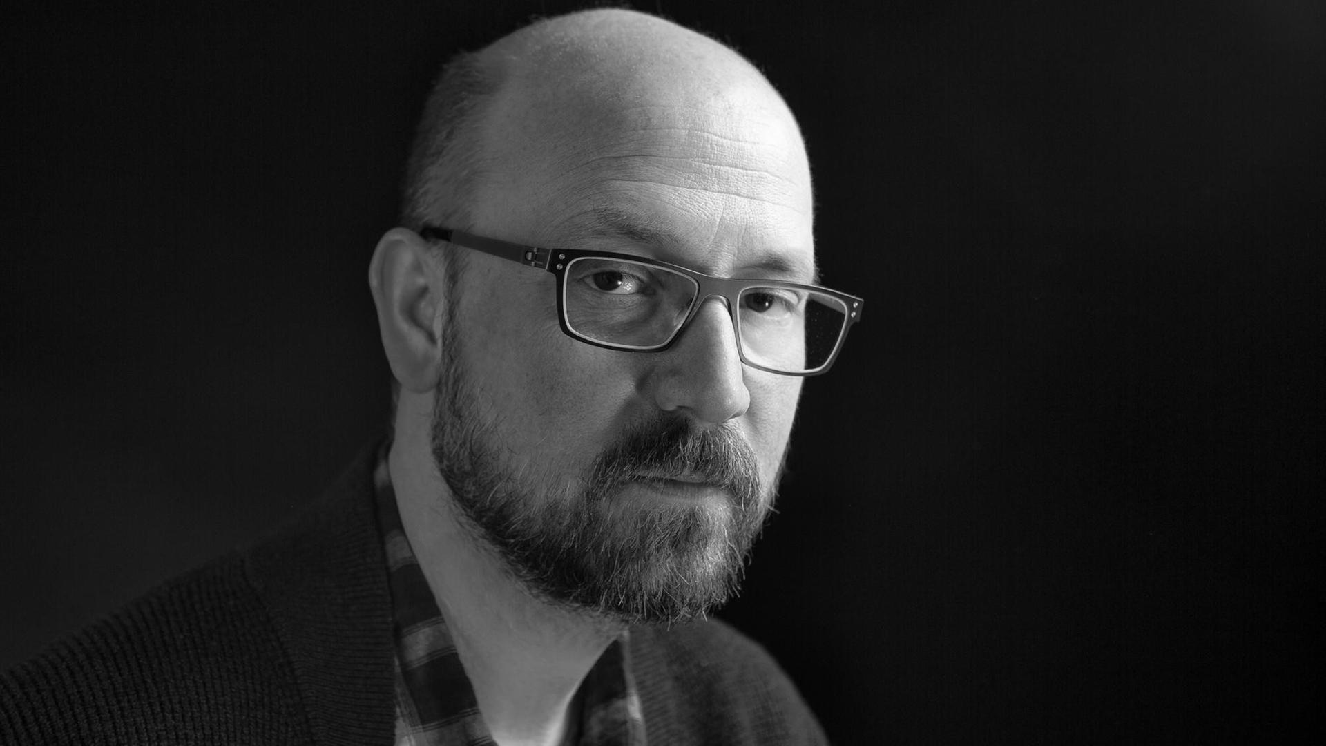 Schwarz-Weiß-Foto von Chip Cheek. Ein Mann mit Glatze, Bart und Brille. Schwarz-Weiß-Foto von Chip Cheek. Ein Mann mit Glatze, Bart und Brille.