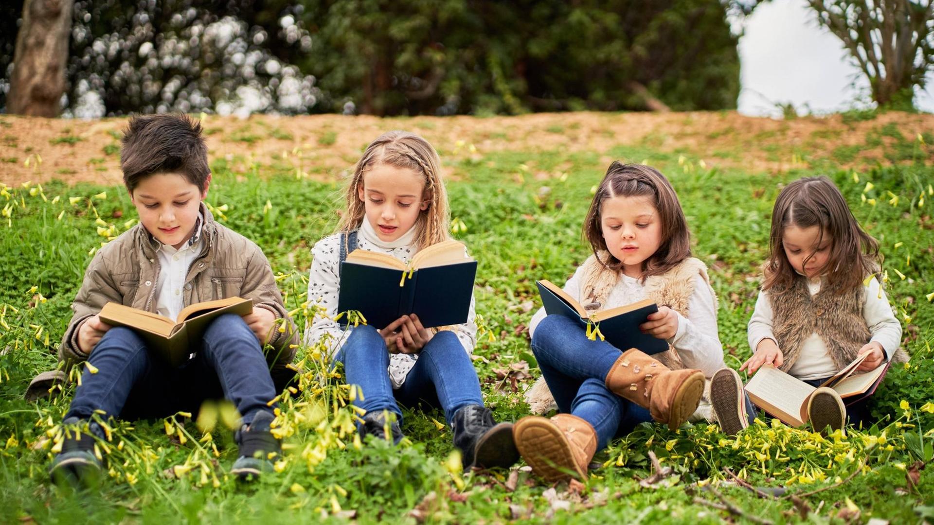 Smart children sitting on green hill in park and reading interesting books while enjoying weekend together Copyright: xDanielxLozanox