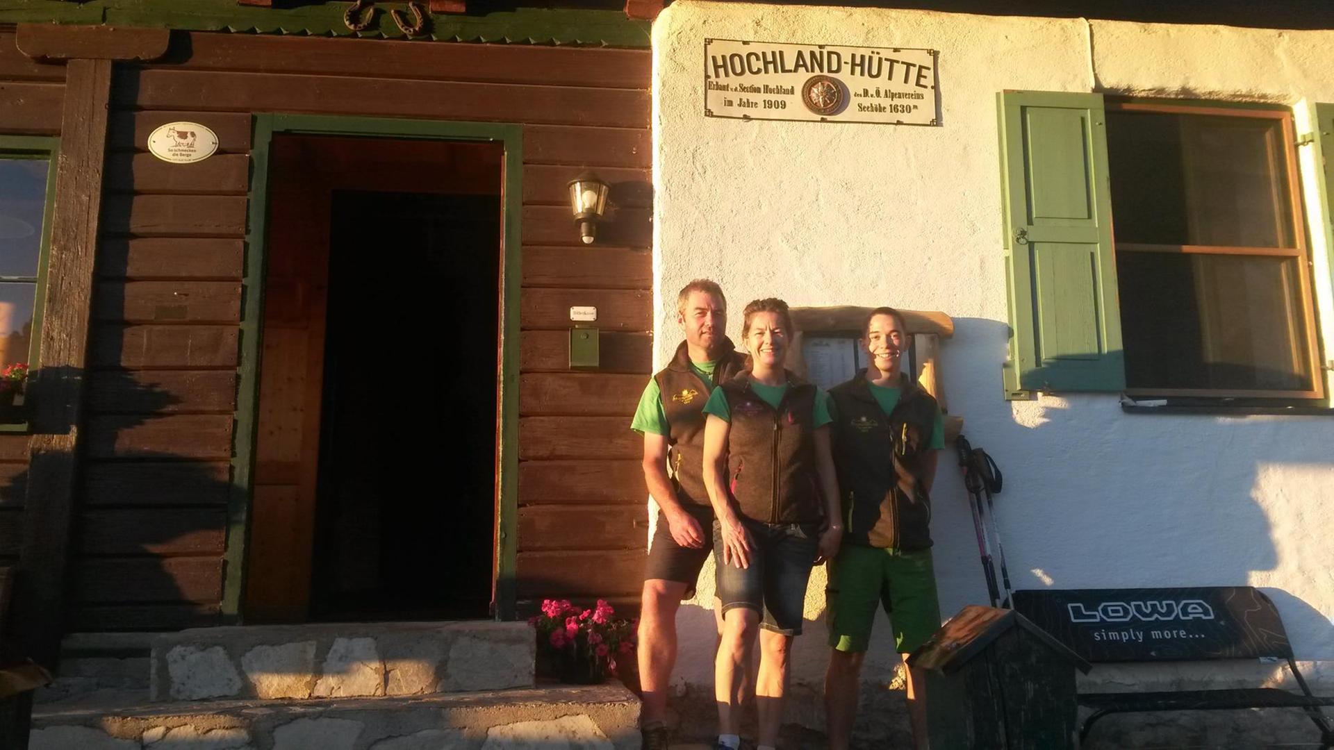 Drei Menschen stehen vor der Hochland-Hütte. Drei Menschen stehen vor der Hochland-Hütte.