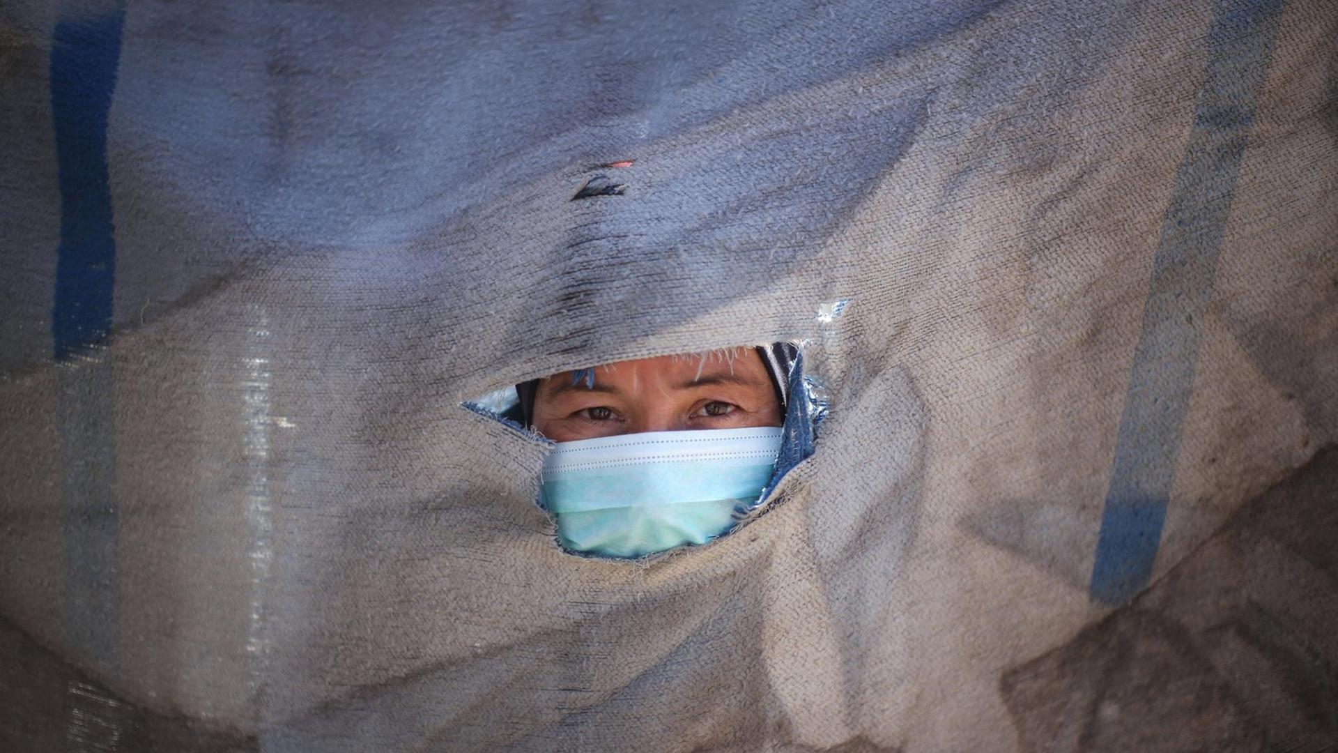 Der Kopf eines Mannes mit Schutzmaske schaut aus einem Loch einem Stück Stoff hervor.