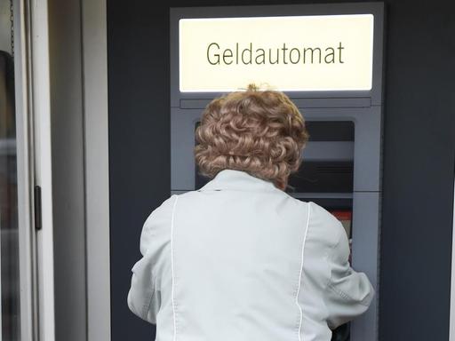 Eine ältere Frau hebt am Geldautomaten einer Sparkassen-Filiale Geld ab.