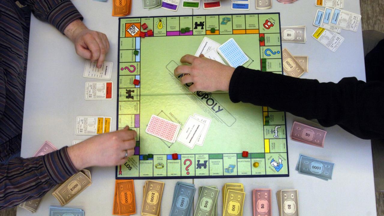 Hände an einem Monopoly-Spielbrett Hände an einem Monopoly-Spielbrett